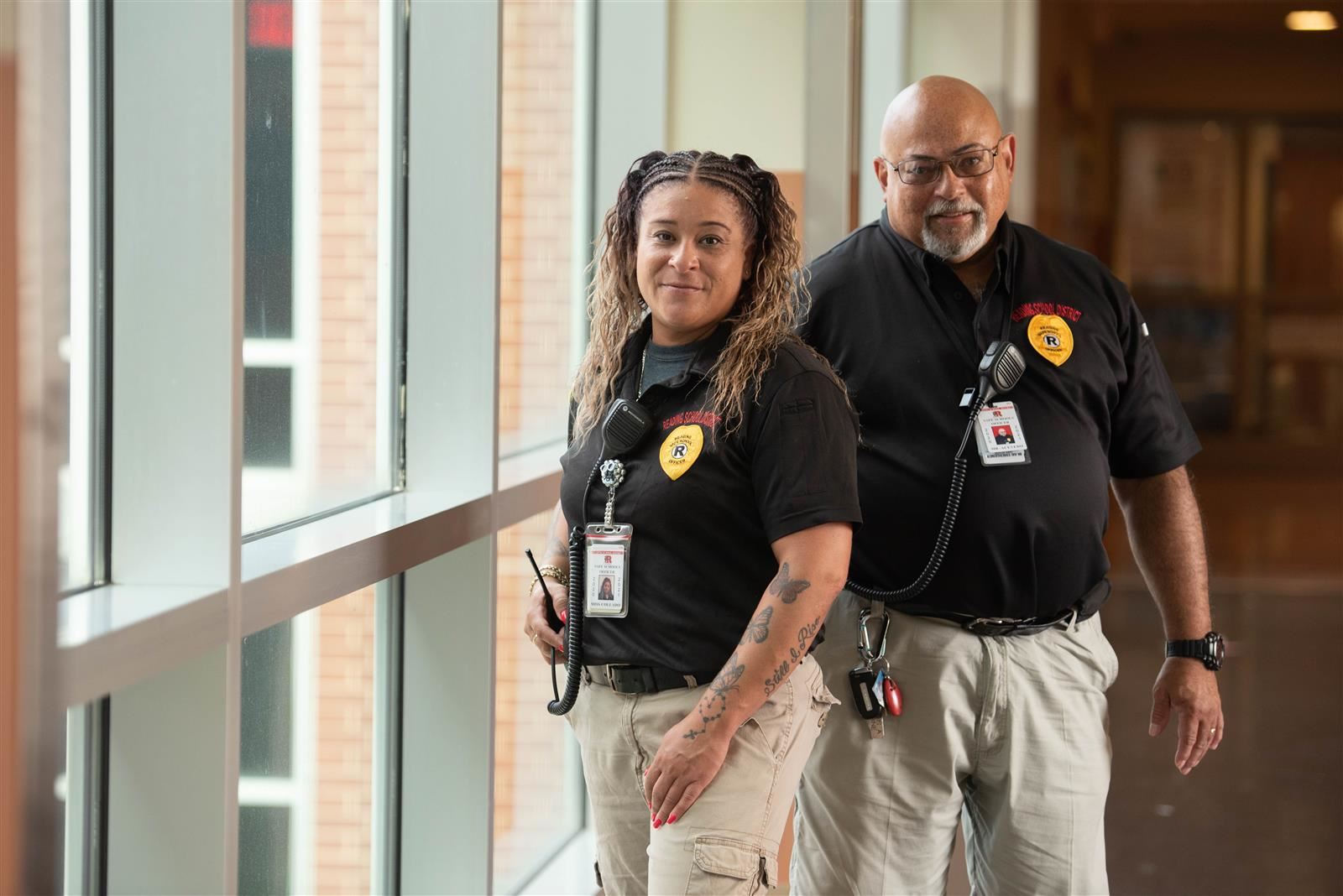 Officers standing outside a building, with the female officer in the foreground looking at something off-camera.