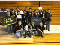 Group of people celebrating their participation in a sports team or event, posing for a photo together with awards and signs.