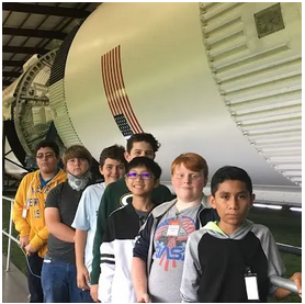 A group of young people posing for a photo in front of a space shuttle.