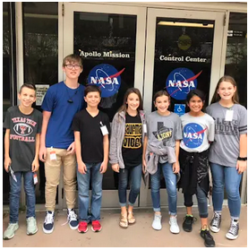 A group of people, including a child, in front of a NASA sign at the entrance of an airport mission control.