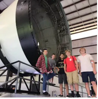 A group of people standing next to a large, circular space shuttle or booster rocket in an indoor exhibit setting.