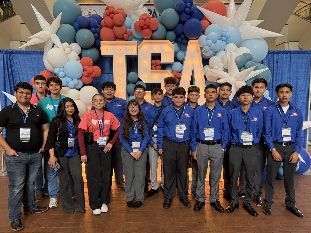 A group of individuals dressed in blue shirts and black pants standing in front of a blue balloon backdrop.