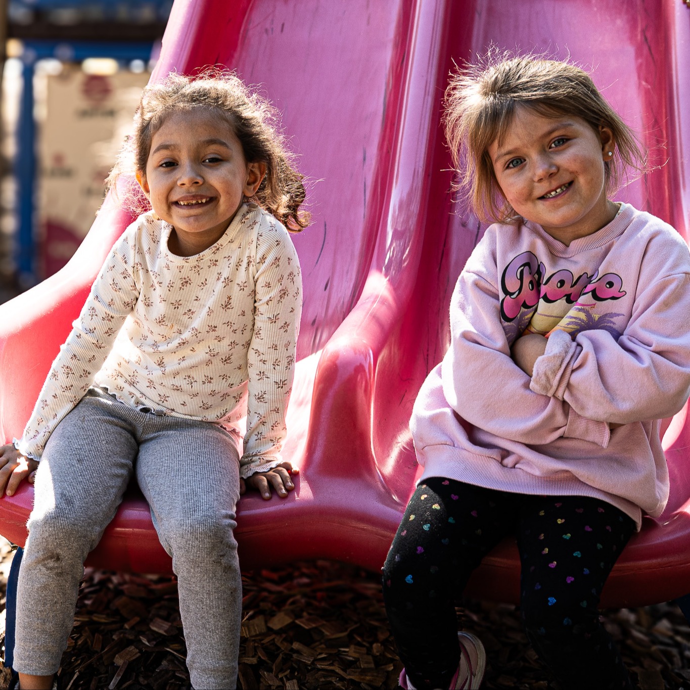 girls sit on the end of a slide, smiling