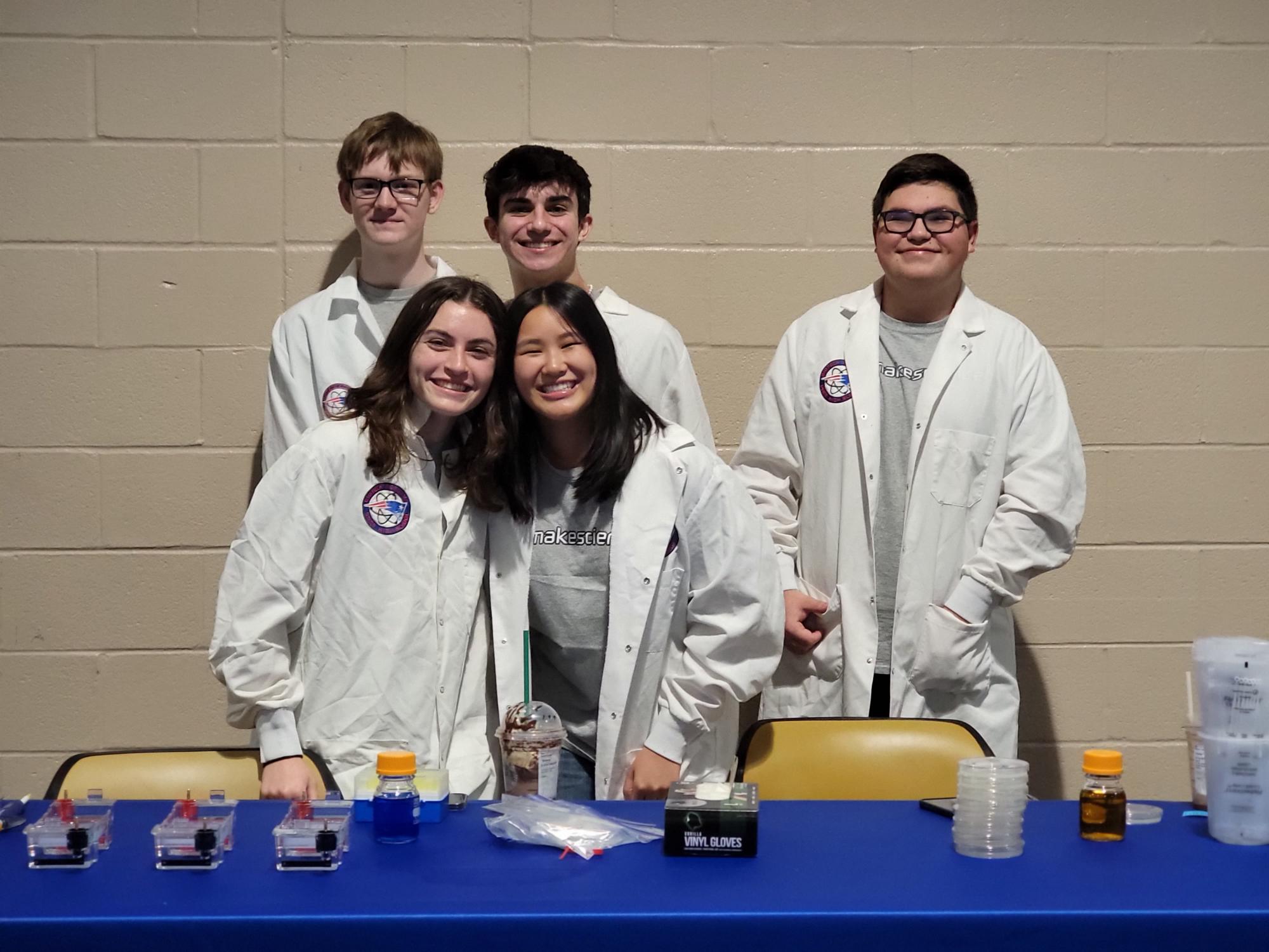 Four young people in lab coats posing together, smiling at the camera.