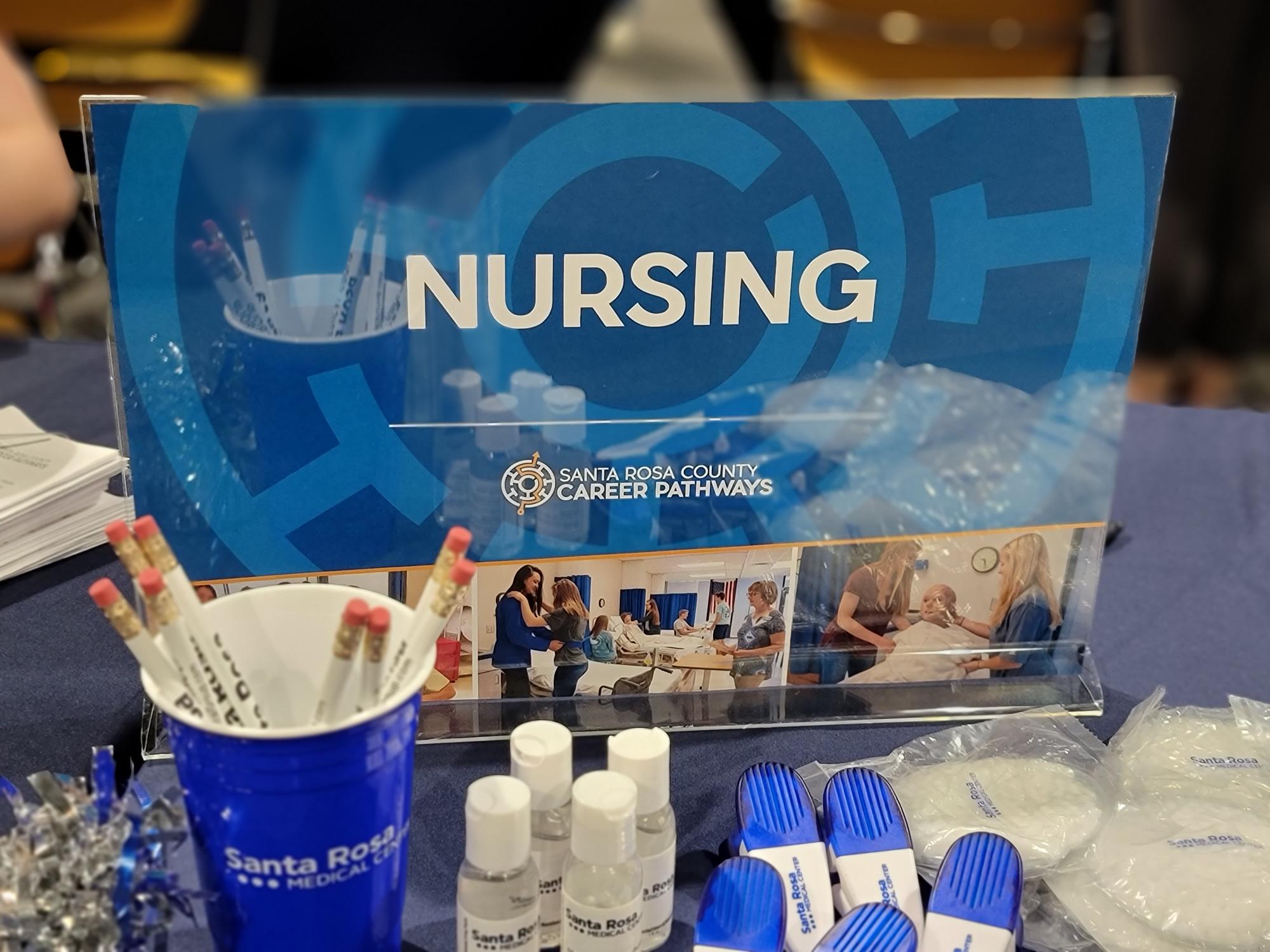 A blue and white sign with the word 'nursing' prominently displayed, accompanied by a table of promotional materials.