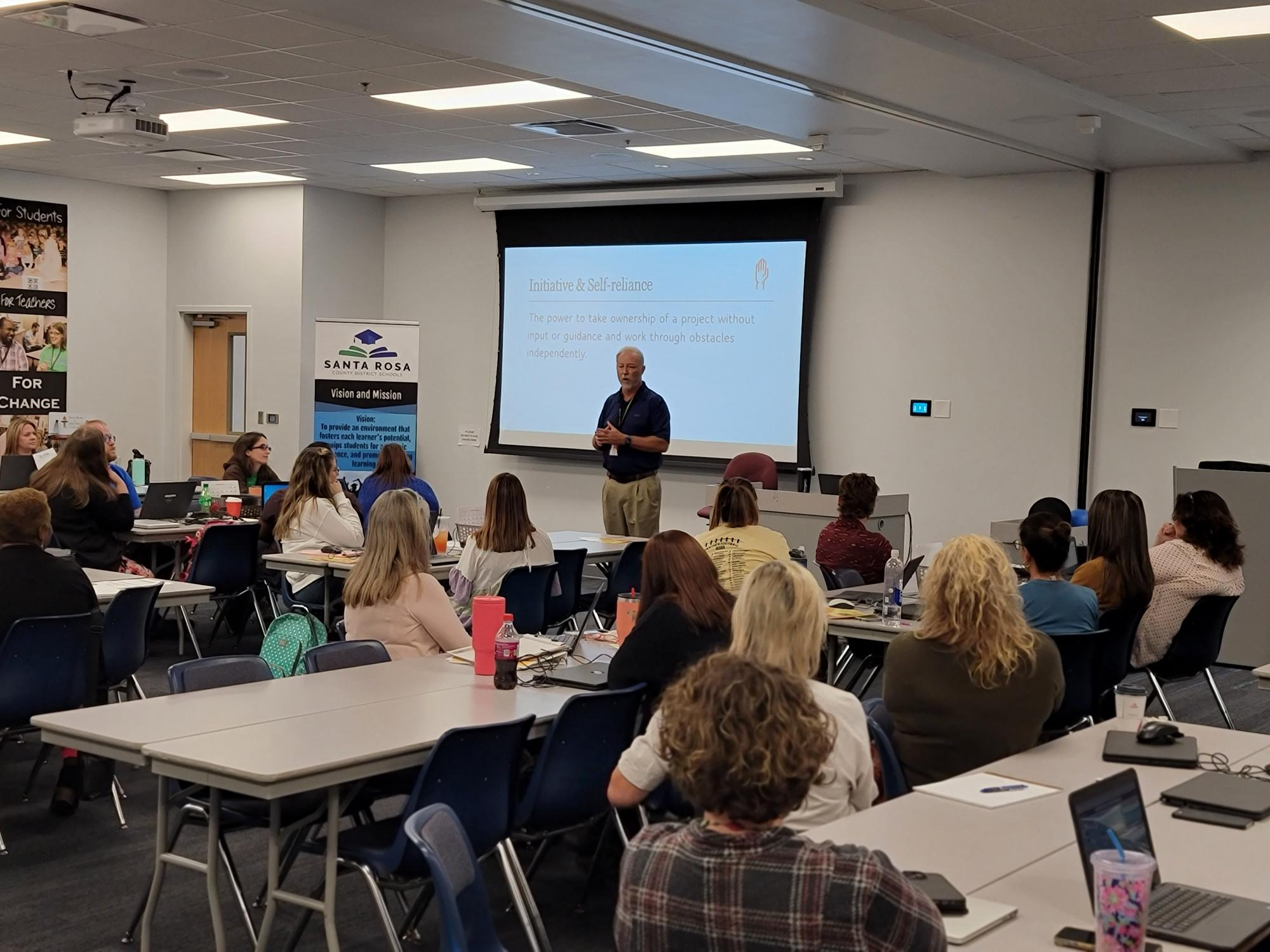 A room full of people gathered for an event or meeting, listening to a speaker.