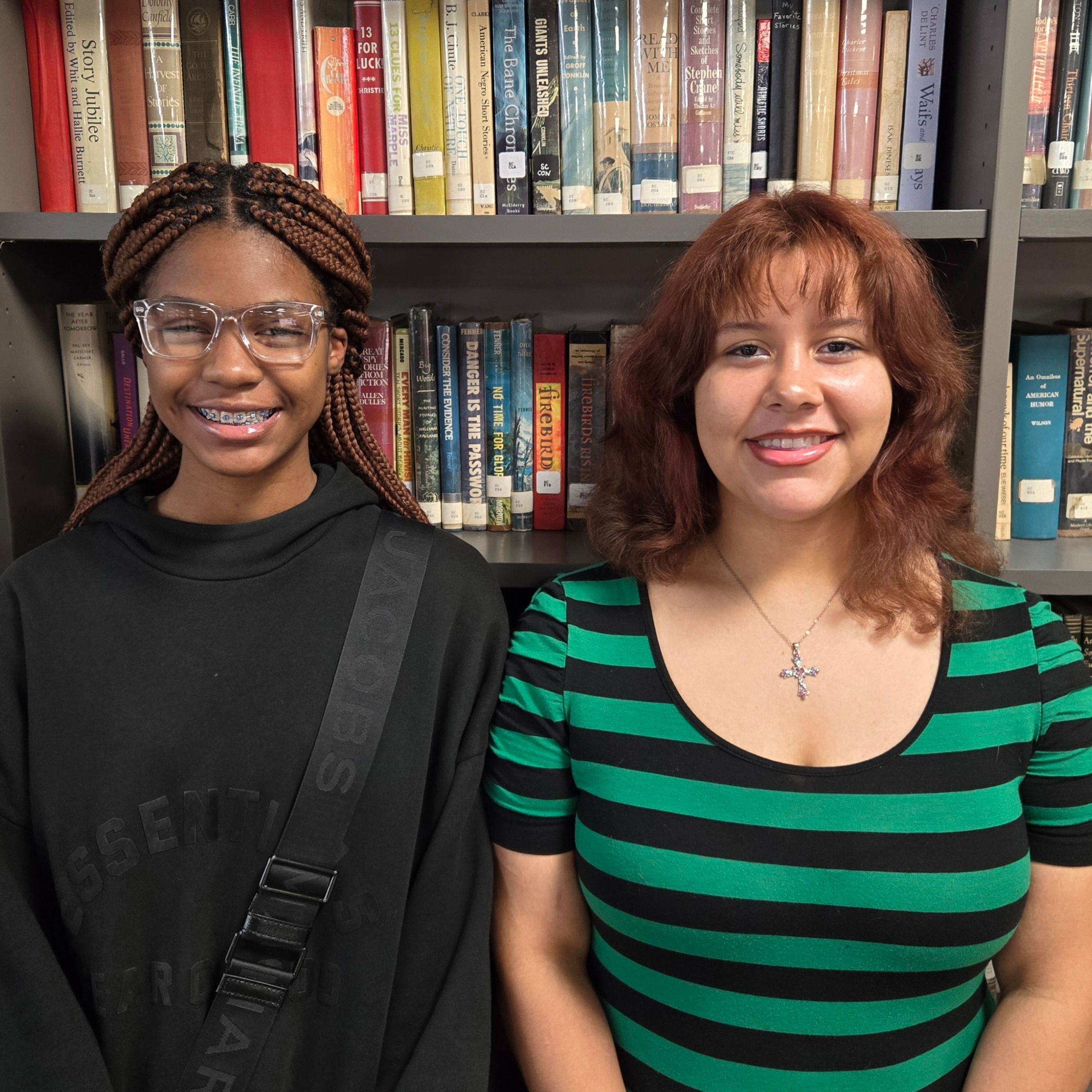 two students standing in front of a wall of books