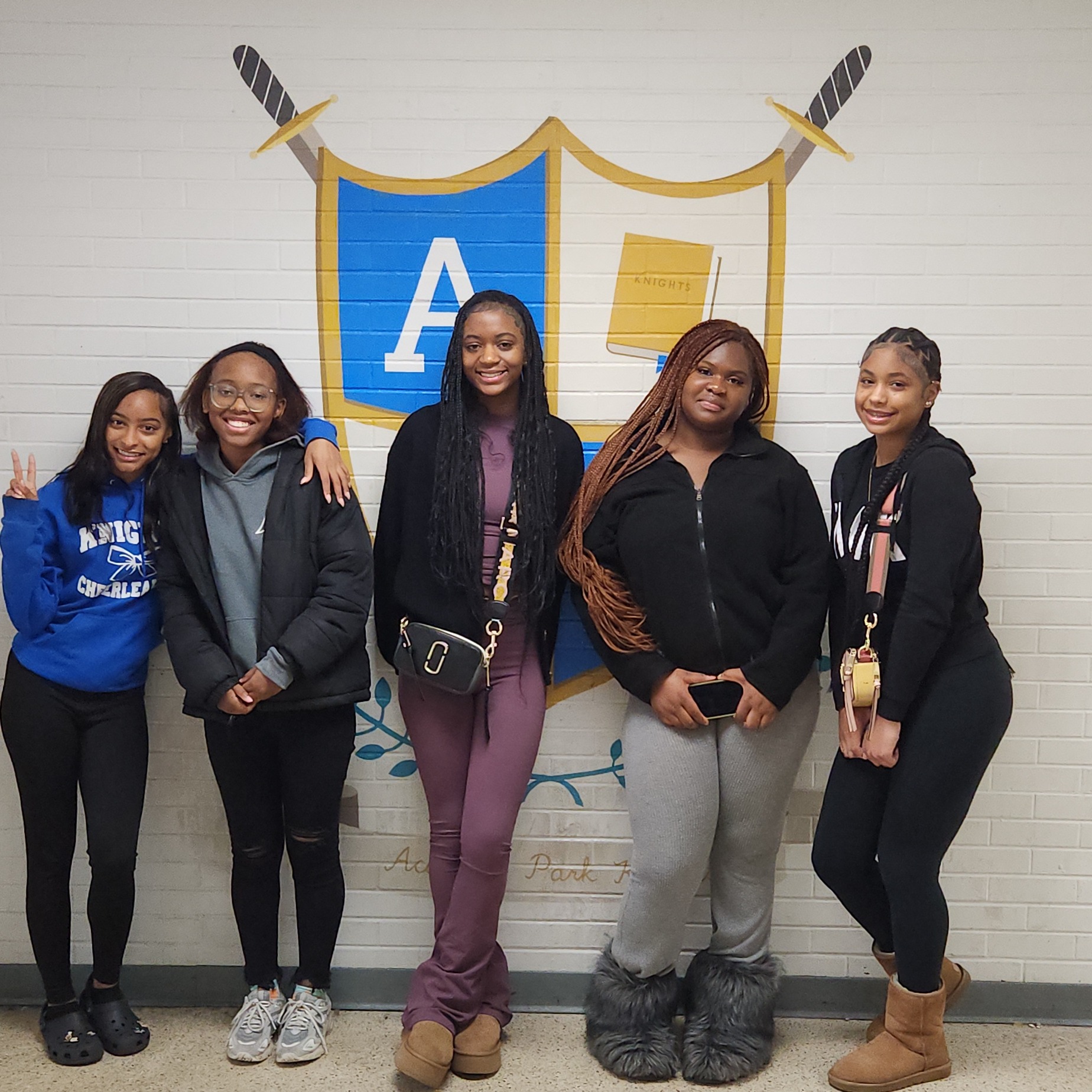 Five female students standing in front of a wall with school shield