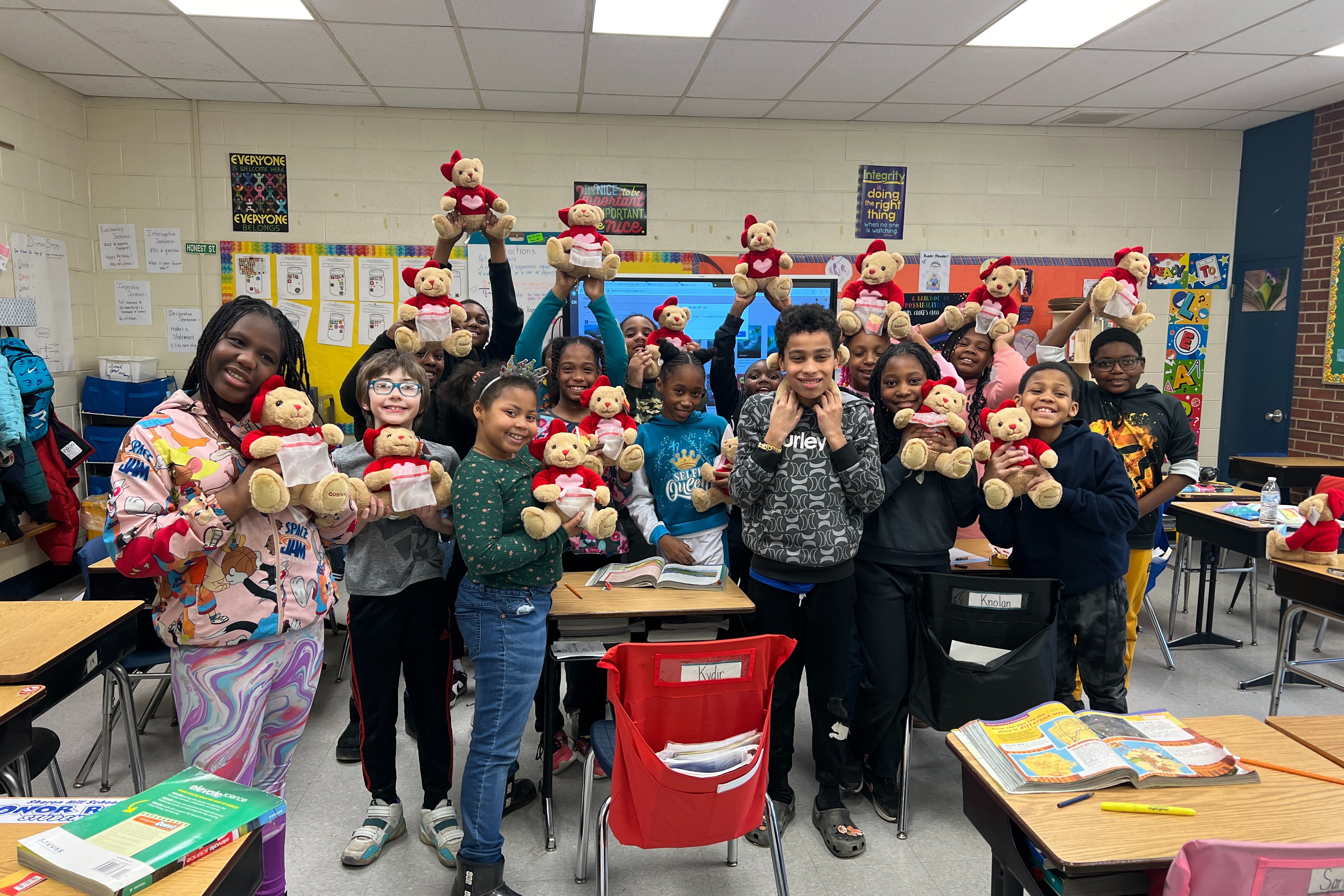 class of students standing and holding a teddy bear