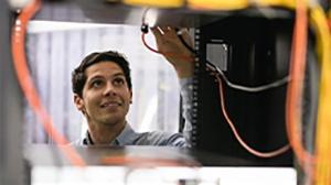 A man is smiling while working on a server rack, adjusting cables and equipment inside.