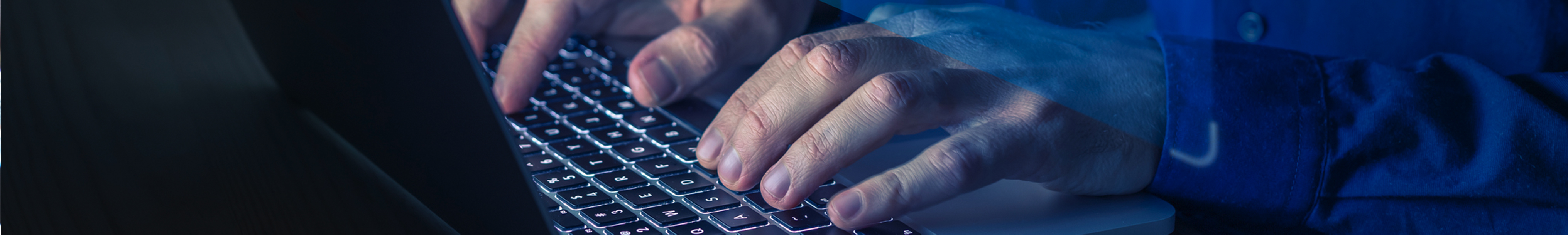 A close-up view of hands typing on a keyboard, with a dark background and blue lighting creating a dramatic effect.