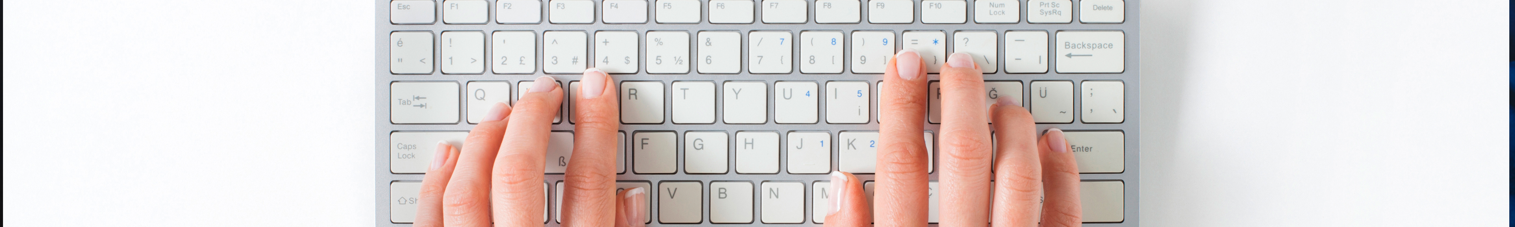 A pair of hands typing on a white keyboard, viewed from above.