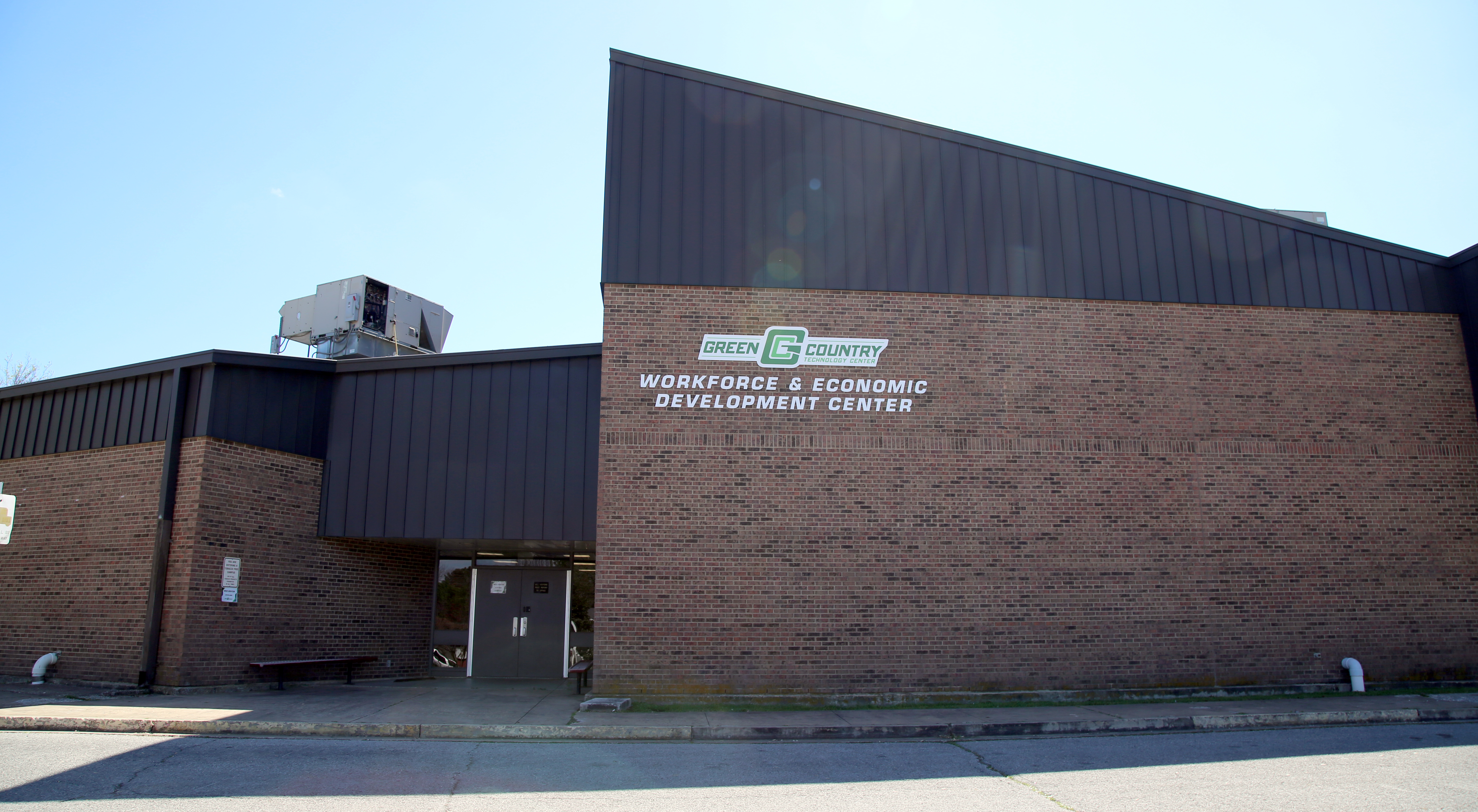 A brick building with a metal roof, featuring a sign that reads 'Manufacturing & Technology Development Center' on the front facade.