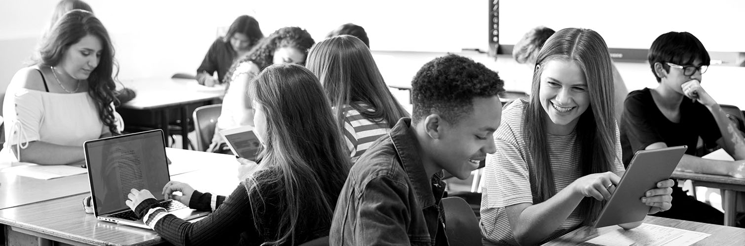 Students in a classroom setting, engaged with laptops and tablets.