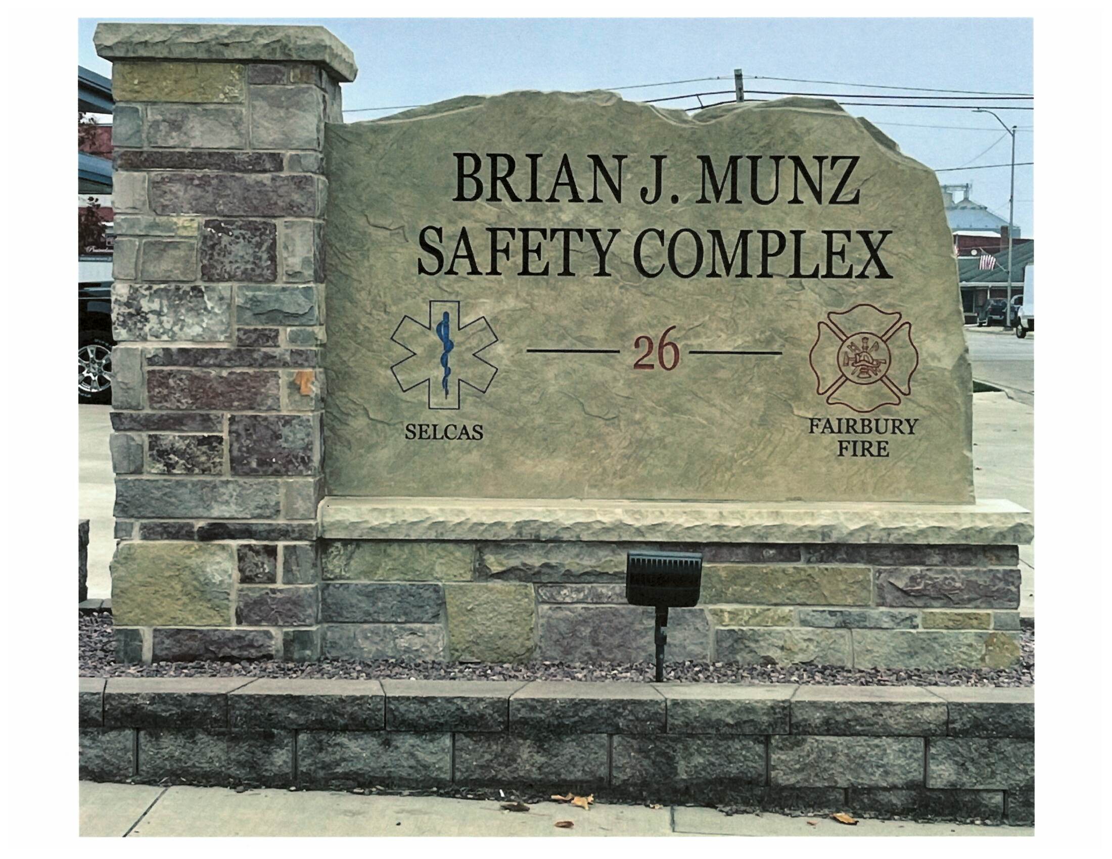 A stone monument displaying the text 'BRIAN J. MUNZ SAFETY COMPLEX' along with symbols representing emergency services and fire department.