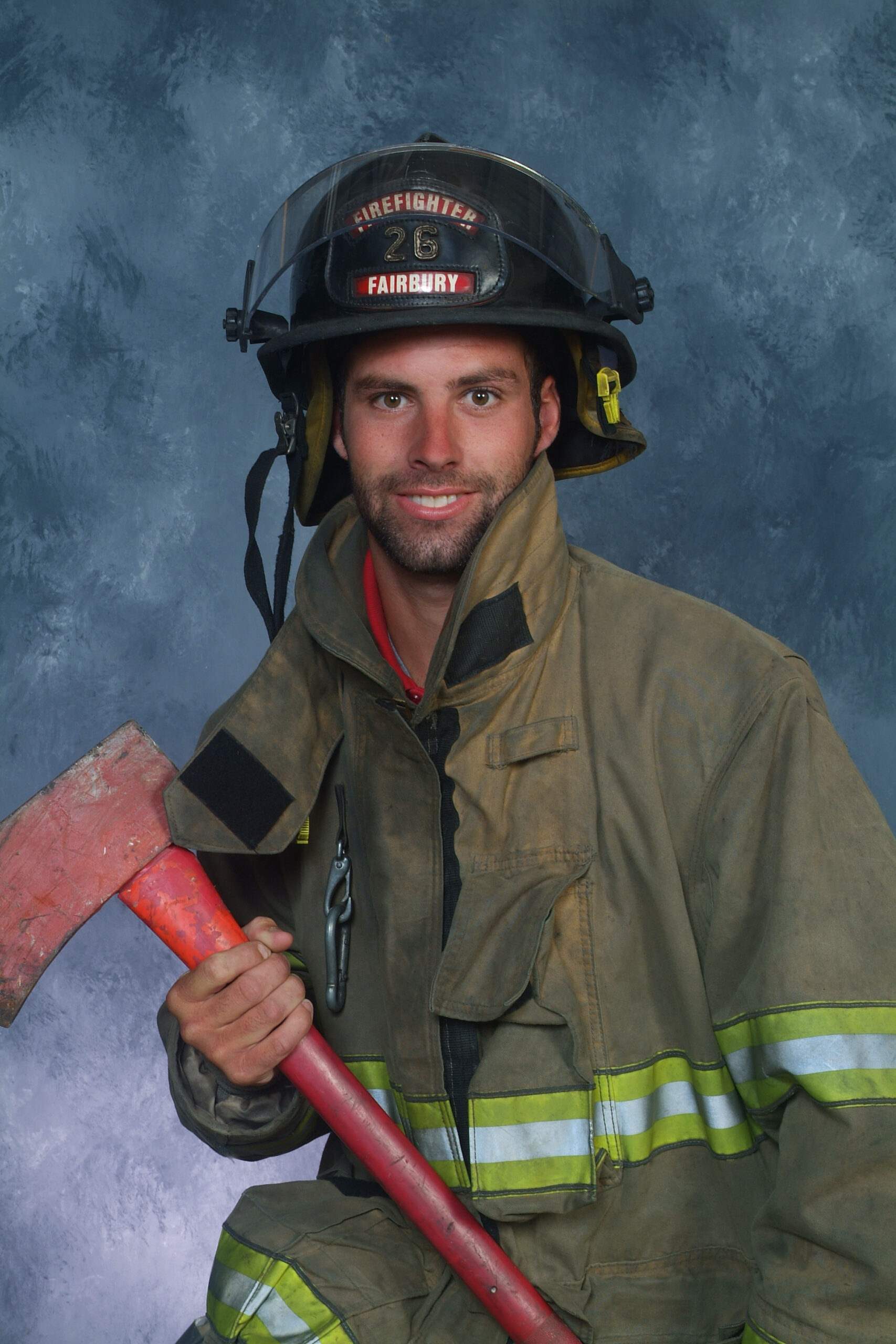 A smiling firefighter in full gear, holding an axe, poses against a textured blue background.