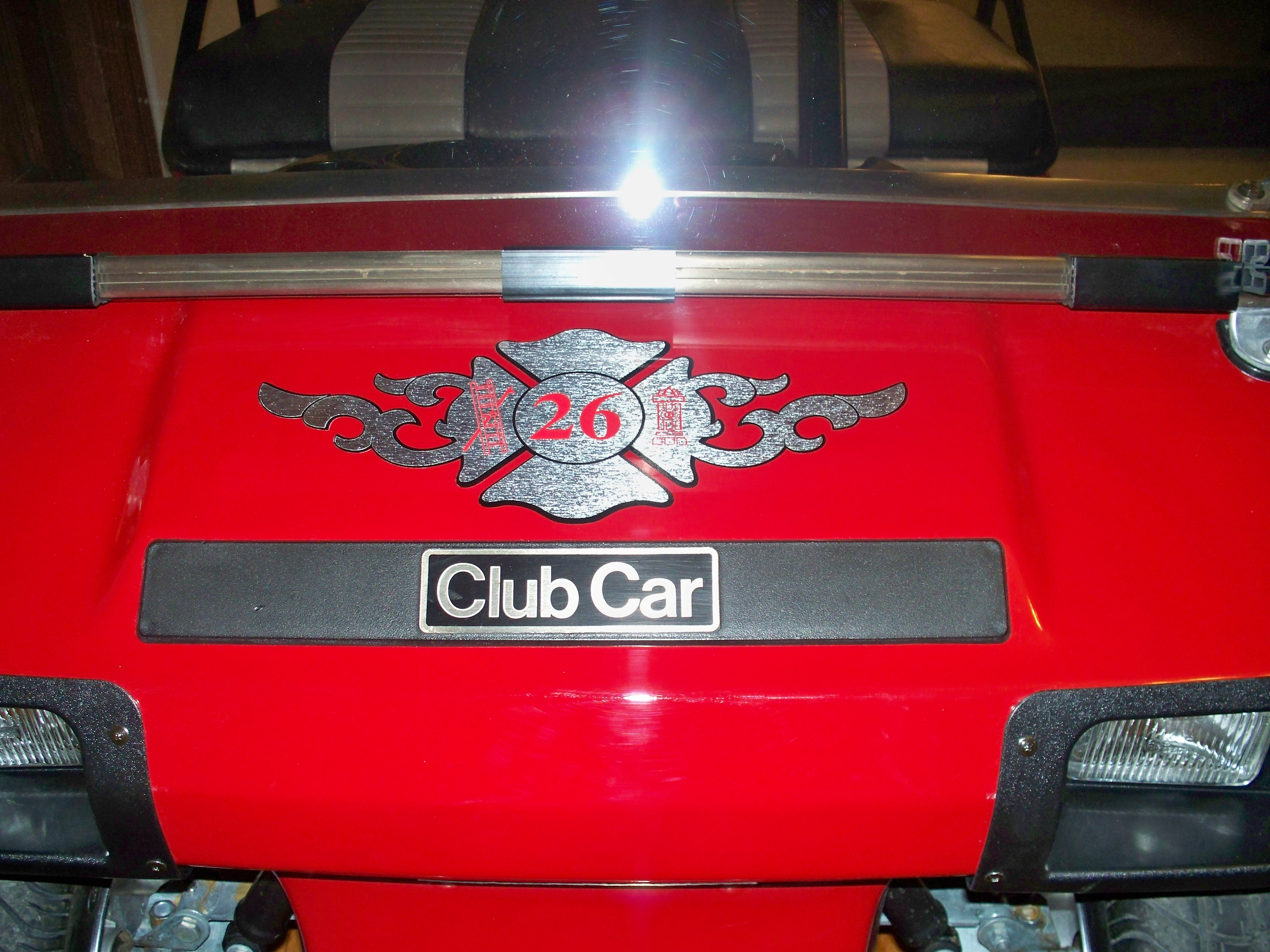 A close-up view of the front of a red golf cart featuring a decorative emblem with the number 26 and the text 'Club Car' prominently displayed.