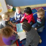 A group of six young children sitting on a colorful rug, engaged in reading a book together.