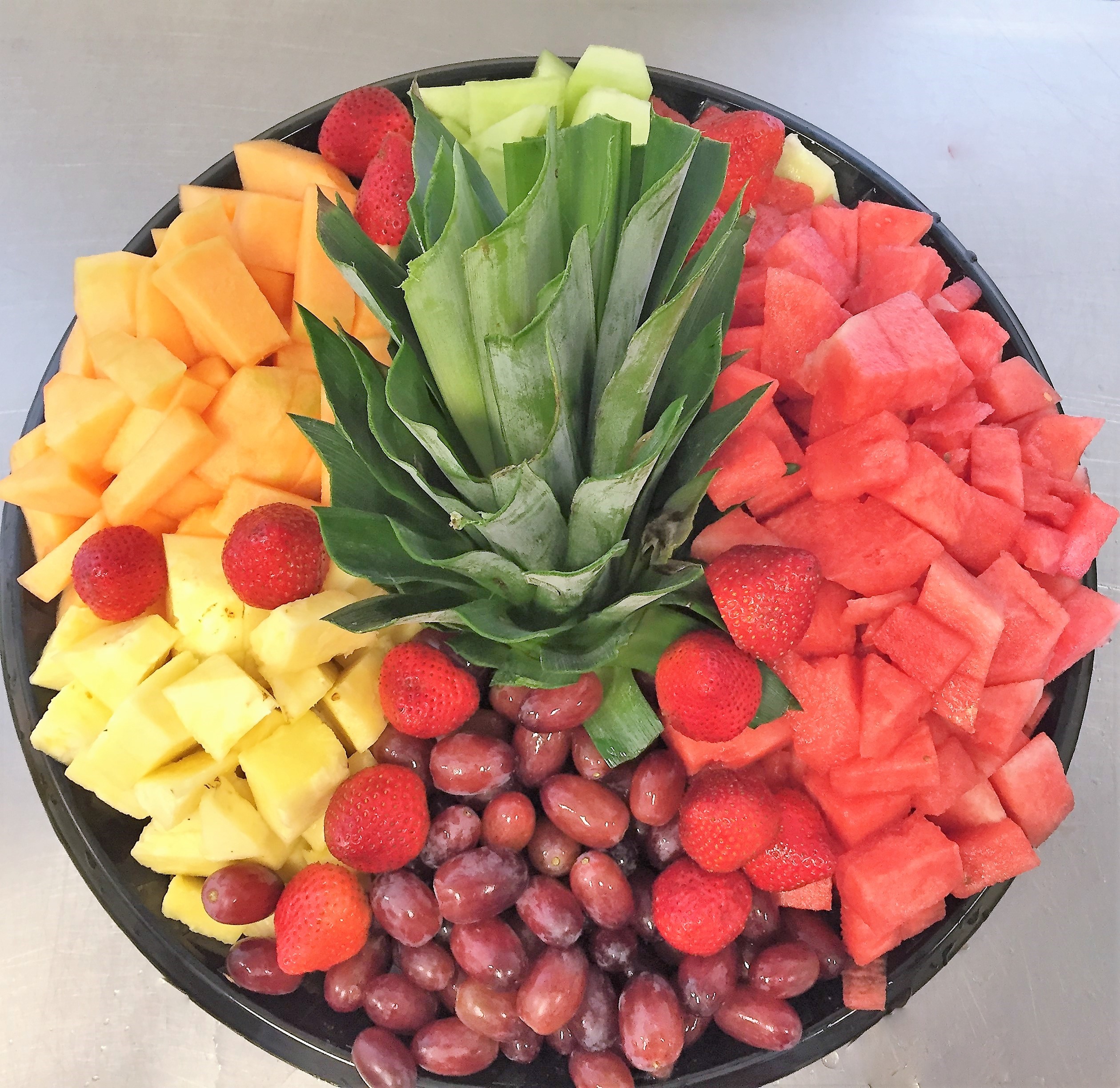 A colorful fruit platter featuring sections of pineapple, watermelon, strawberries, grapes, cantaloupe, and honeydew arranged in a circular design.