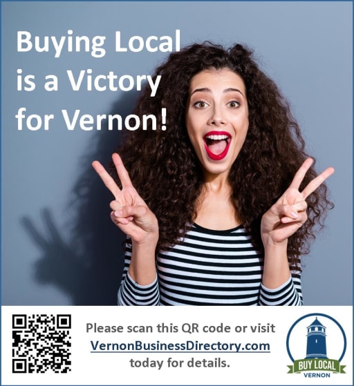 A woman with curly hair smiles and makes a peace sign with both hands, promoting the message 'Buying Local is a Victory for Vernon!' alongside a QR code and website link for more information.