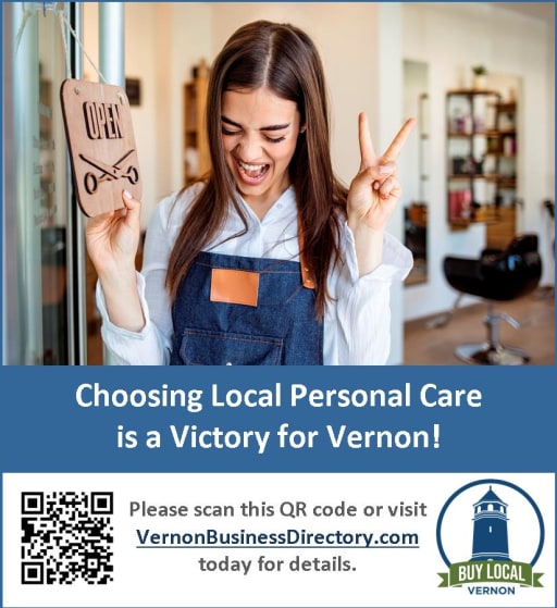 A young woman with long hair smiles and holds an 'Open' sign while giving a thumbs-up in a salon setting, promoting local personal care in Vernon.
