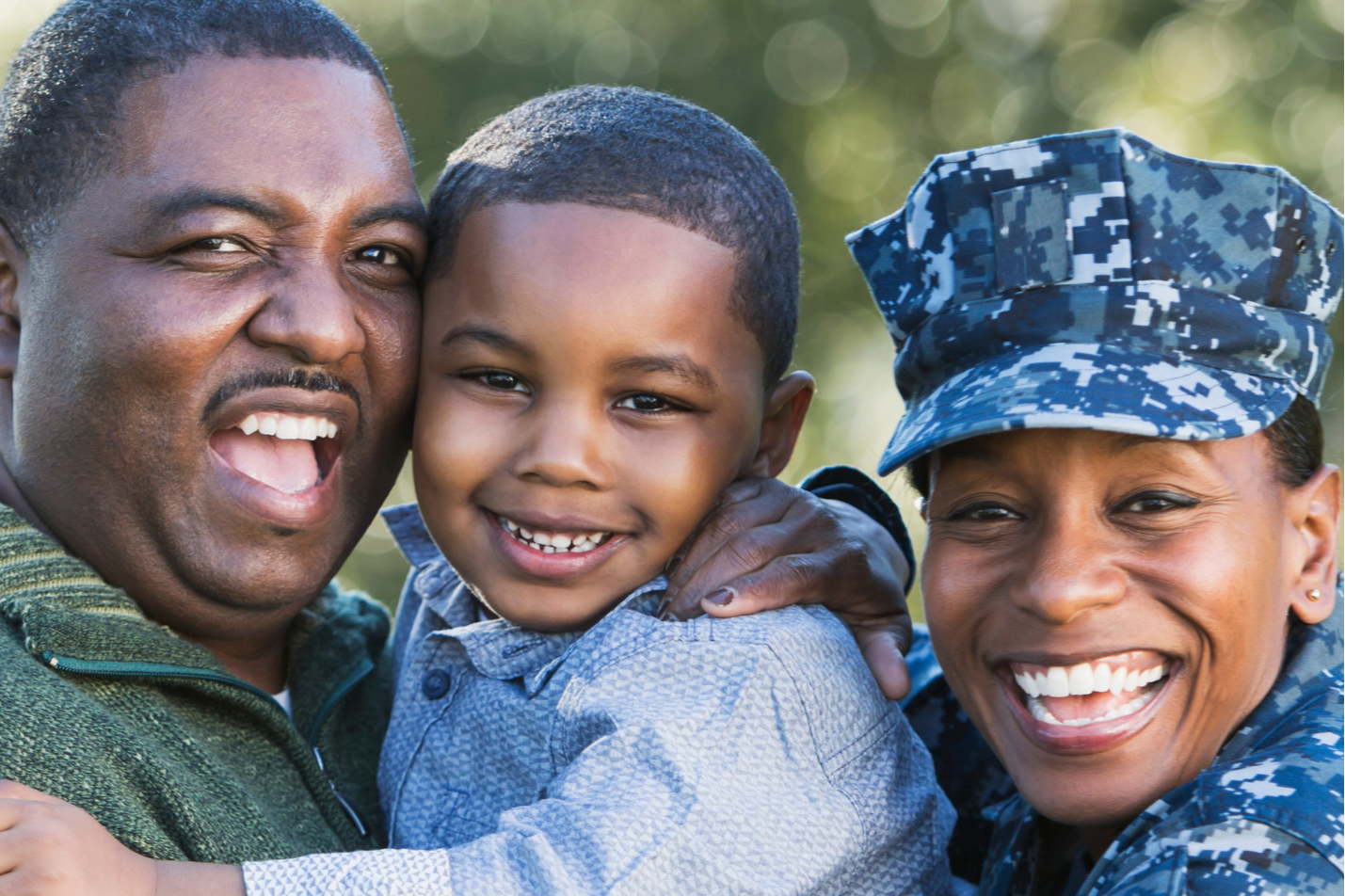 Three people smiling. A man and woman holding a smiling child. The woman is in military uniform.