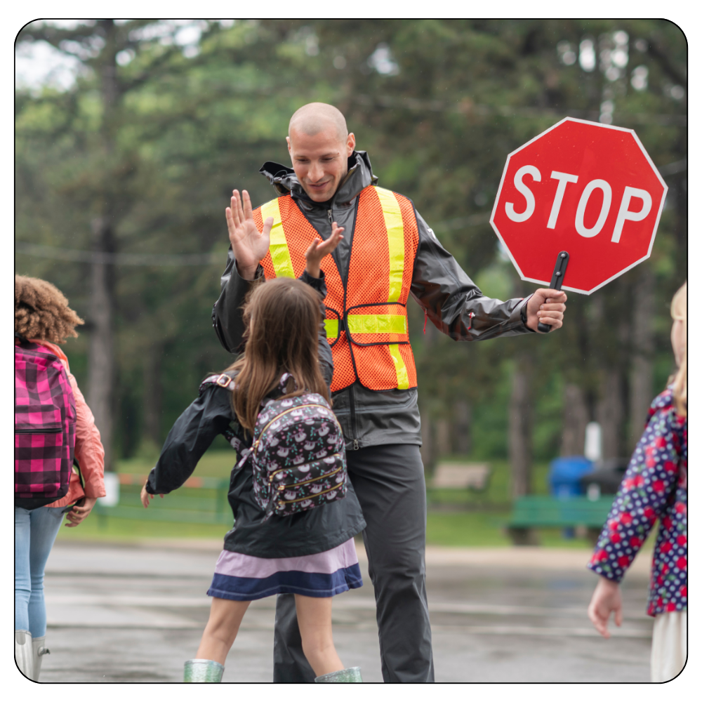 Students crossing the street along with a man holding a stop signal