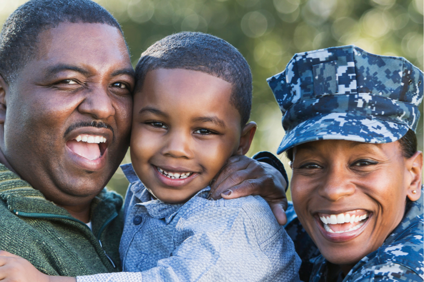 A family of three smiling, with a man in green and a woman in navy uniform, holding a boy.
