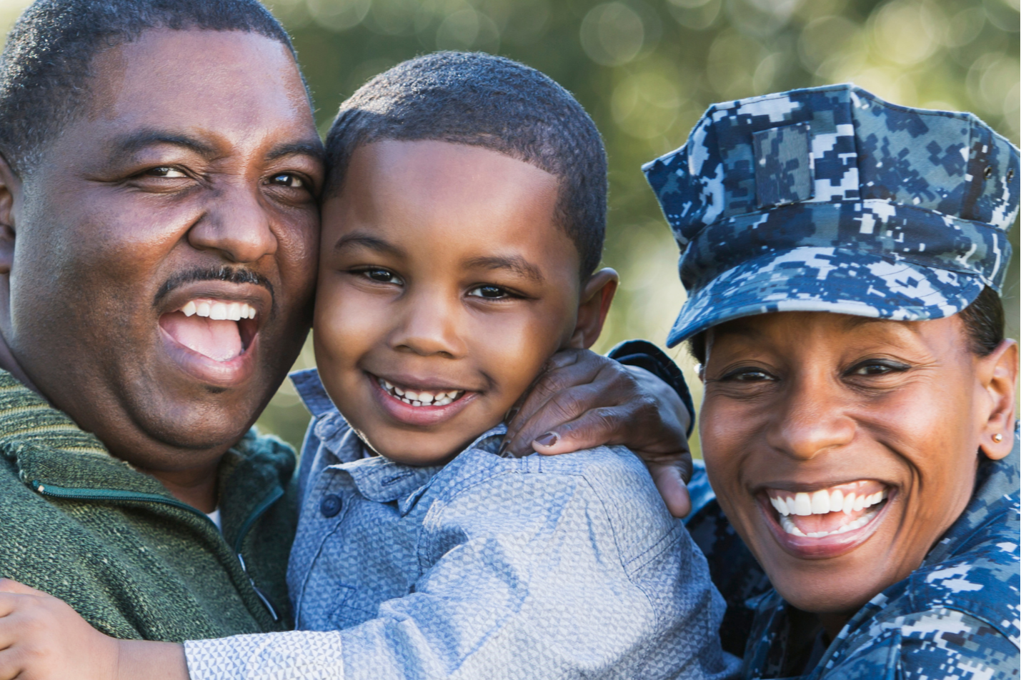 Three individuals smiling, a young boy held by an adult man and woman in a navy blue uniform.