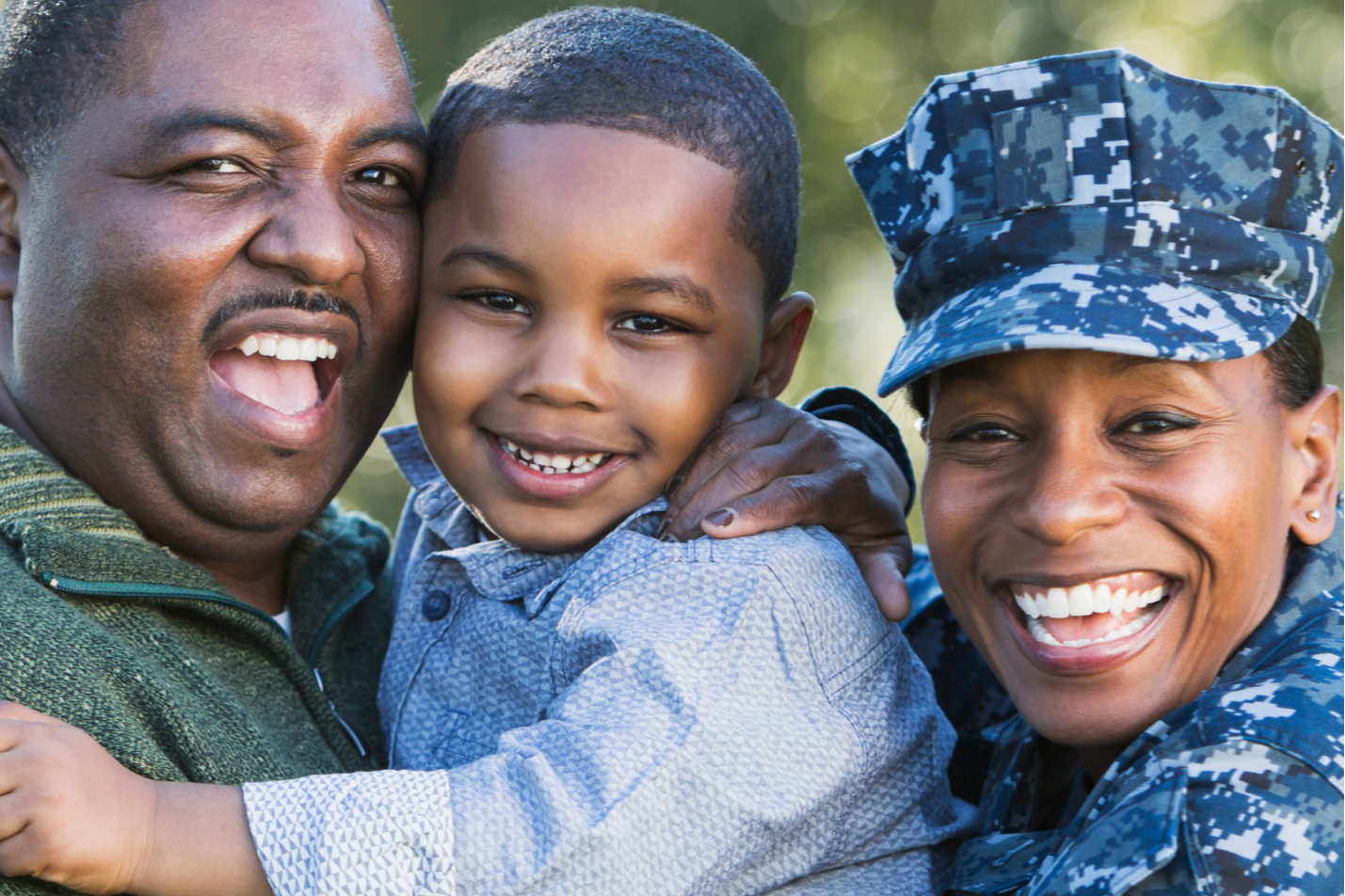 A man, woman, and young child smiling and hugging. The woman is in a military uniform.