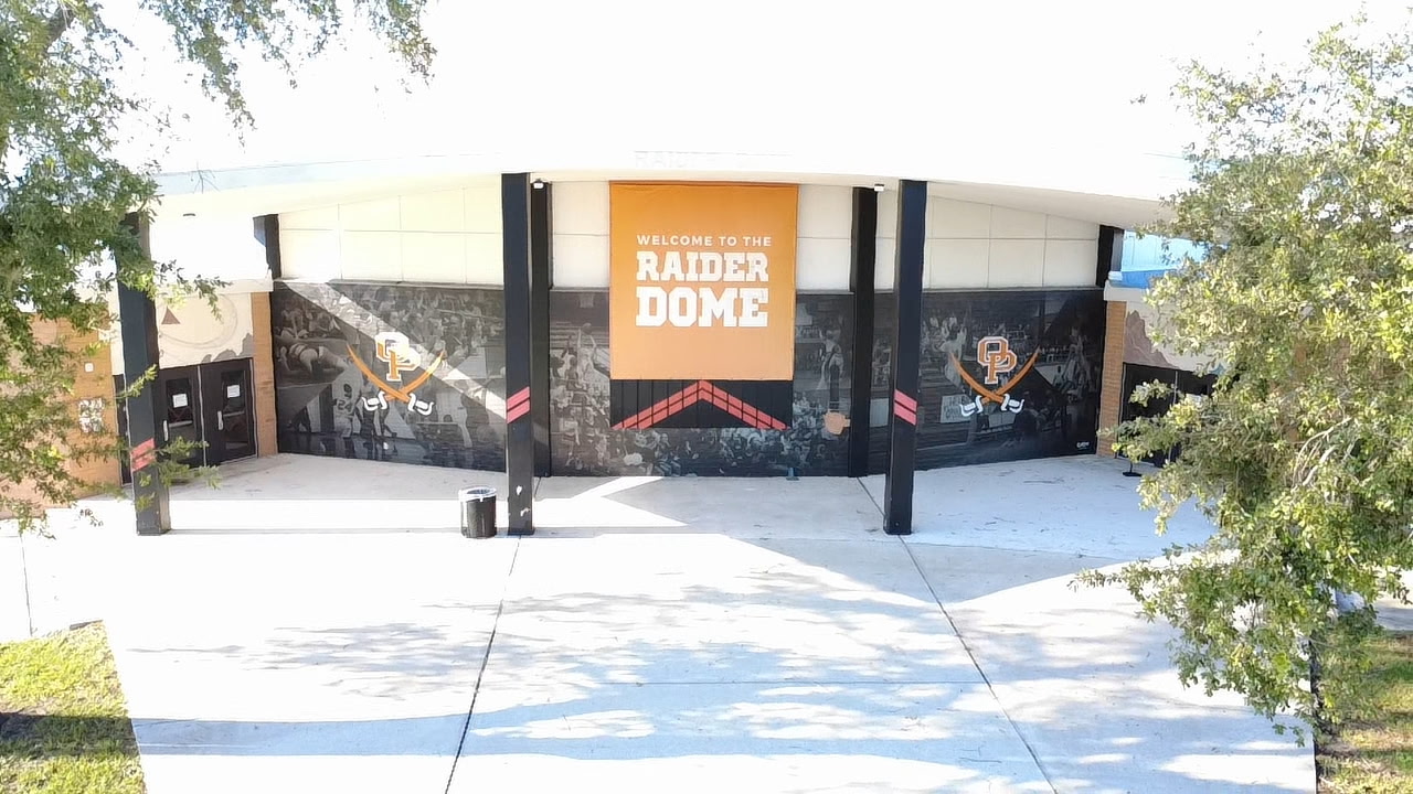 Exterior of a sports facility with a large banner reading "RAIDER DOME" and colorful murals on a white and black wall.