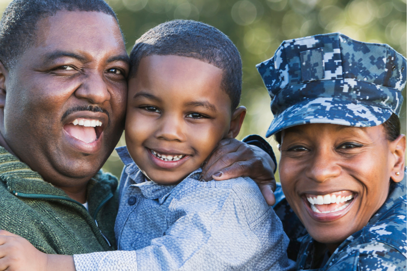 A man, woman, and child in military uniforms, smiling and holding a child outdoors.