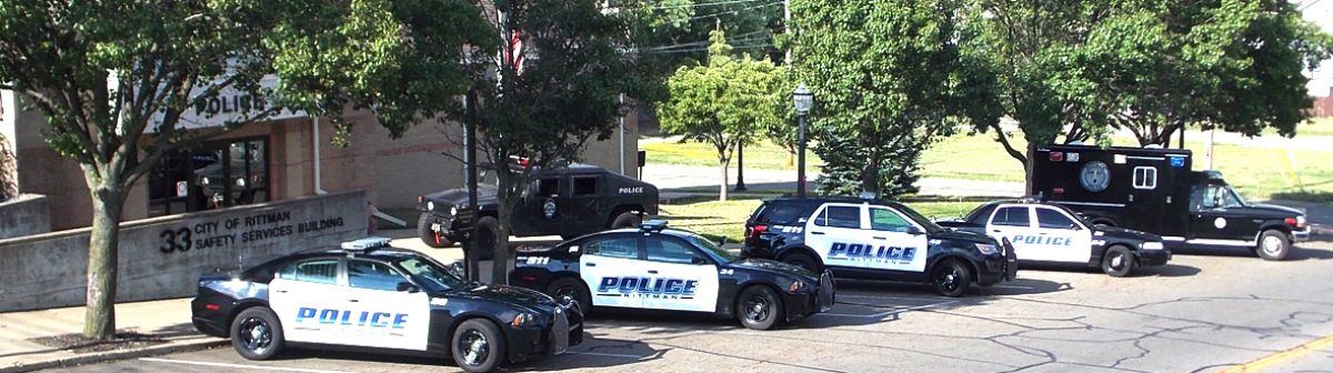 A lineup of several police vehicles parked outside a building, surrounded by trees.