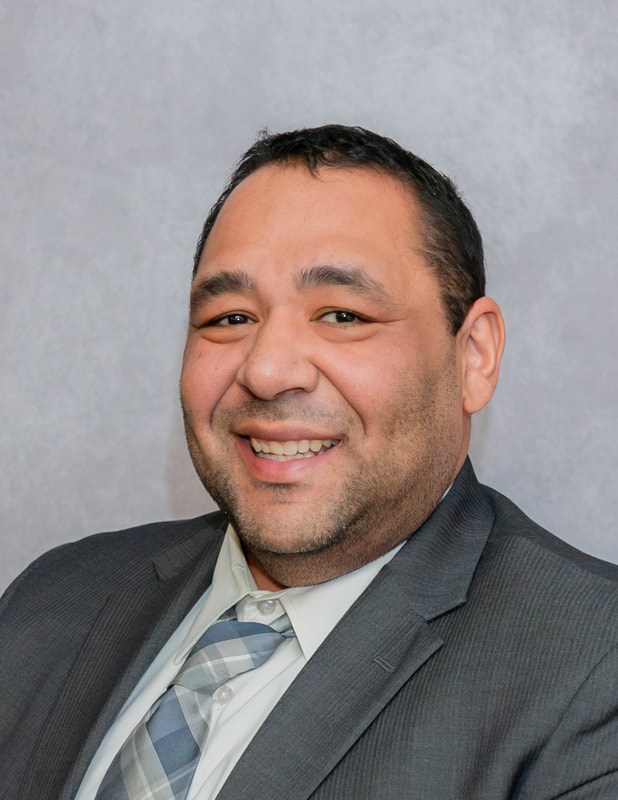 A smiling man in a suit and tie poses against a gray background.