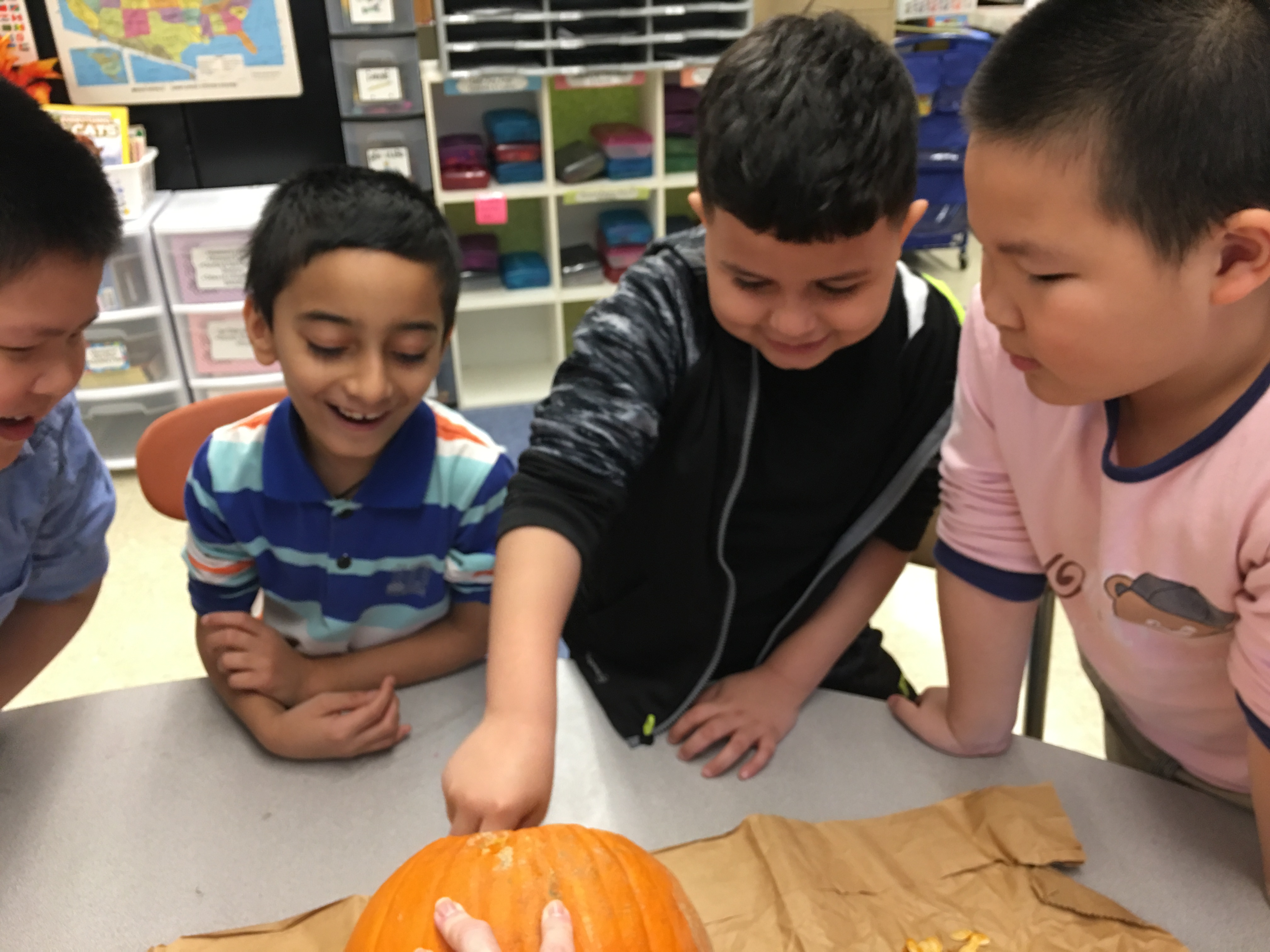 Four children are gathered around a table, eagerly examining a pumpkin, with one child reaching into it while the others watch with smiles.