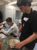 Two young individuals are engaged in a cooking activity, with one stirring a bowl of batter while the other is working on a separate task in the background.