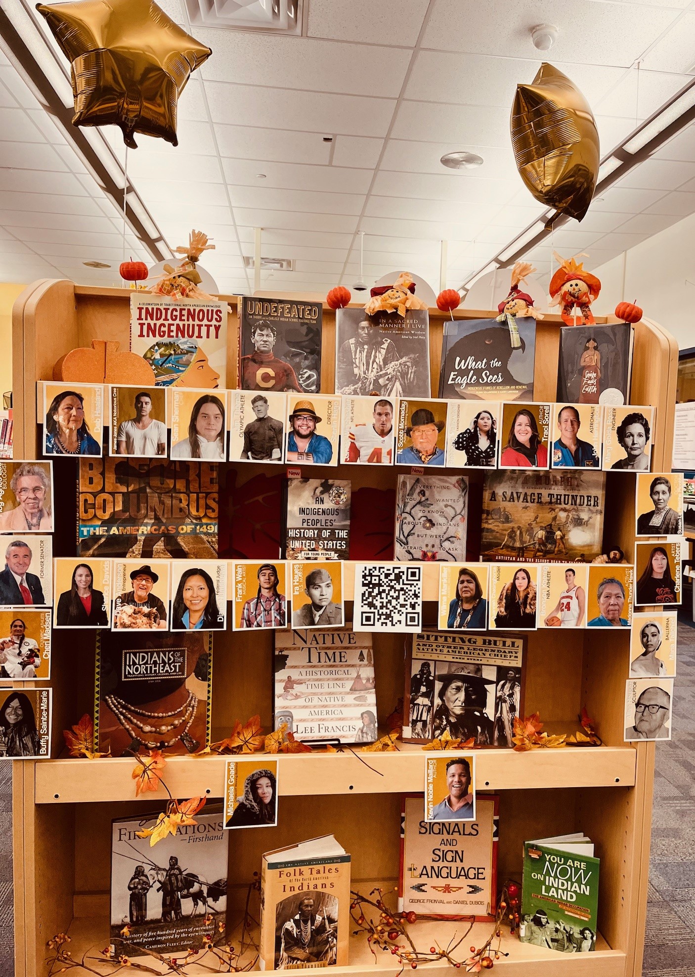 A display shelf featuring various books and portraits of diverse authors, decorated with balloons and festive elements, set in a library or community space.