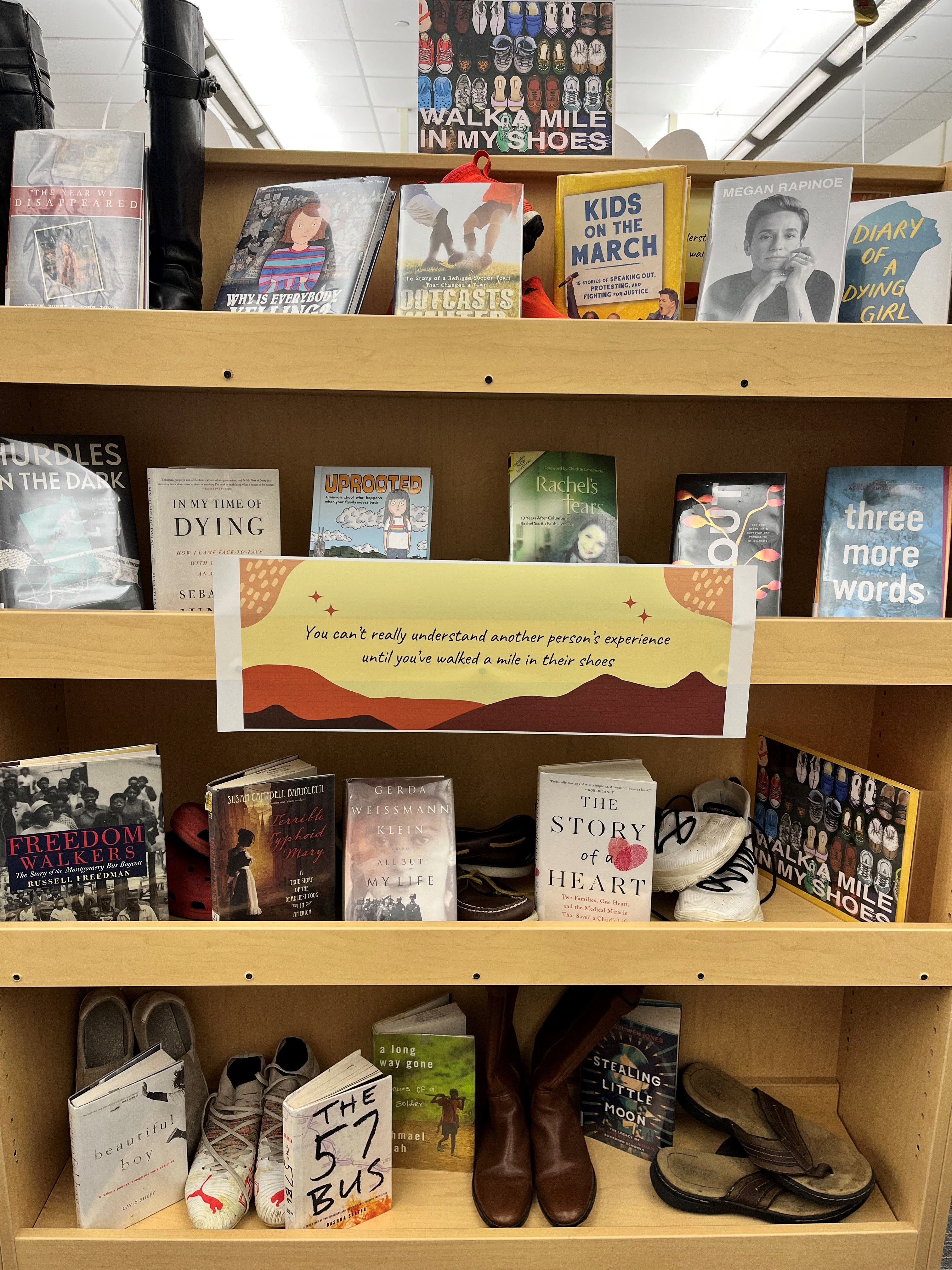A wooden bookshelf displaying various books and a pair of boots, with a sign in the center promoting a reading theme.