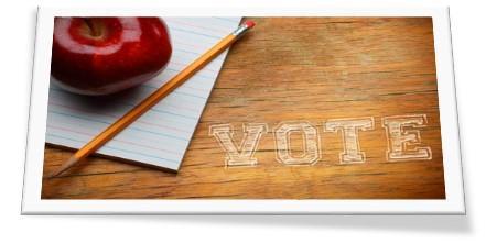 A red apple and a pencil are placed on a wooden surface next to a sheet of lined paper, with the word 'VOTE' written in a chalk-like font on the wood.