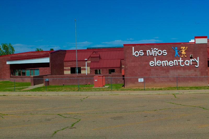 A brick building with the sign 'los niños elementary' displayed prominently on the front, set against a clear blue sky.