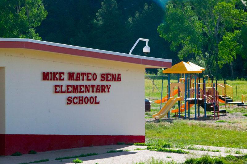 A view of the Mike Mateo Sena Elementary School building with a playground in the background, surrounded by greenery.