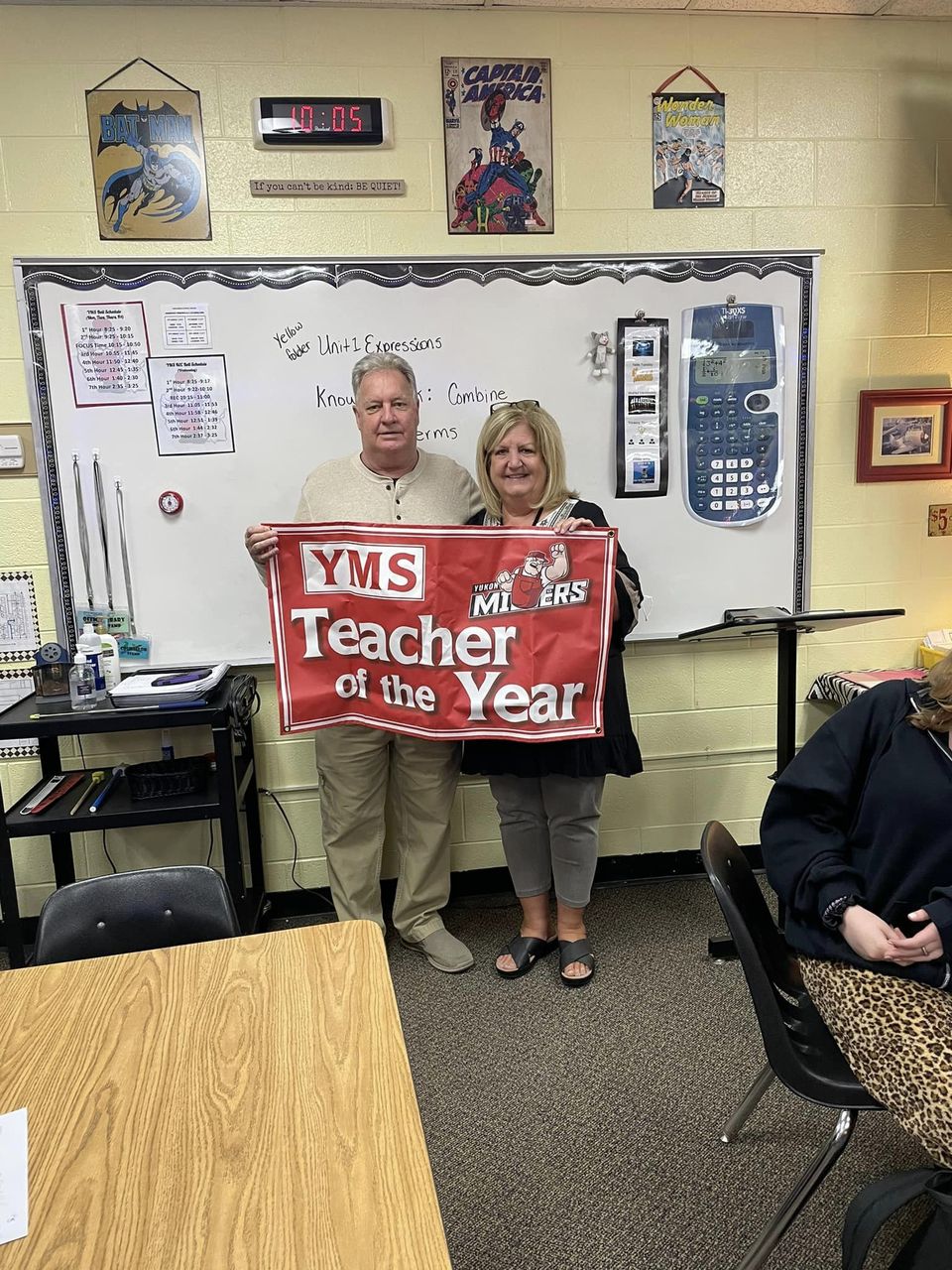 Two educators stand together in a classroom holding a banner that reads 'YMS Teacher of the Year.'