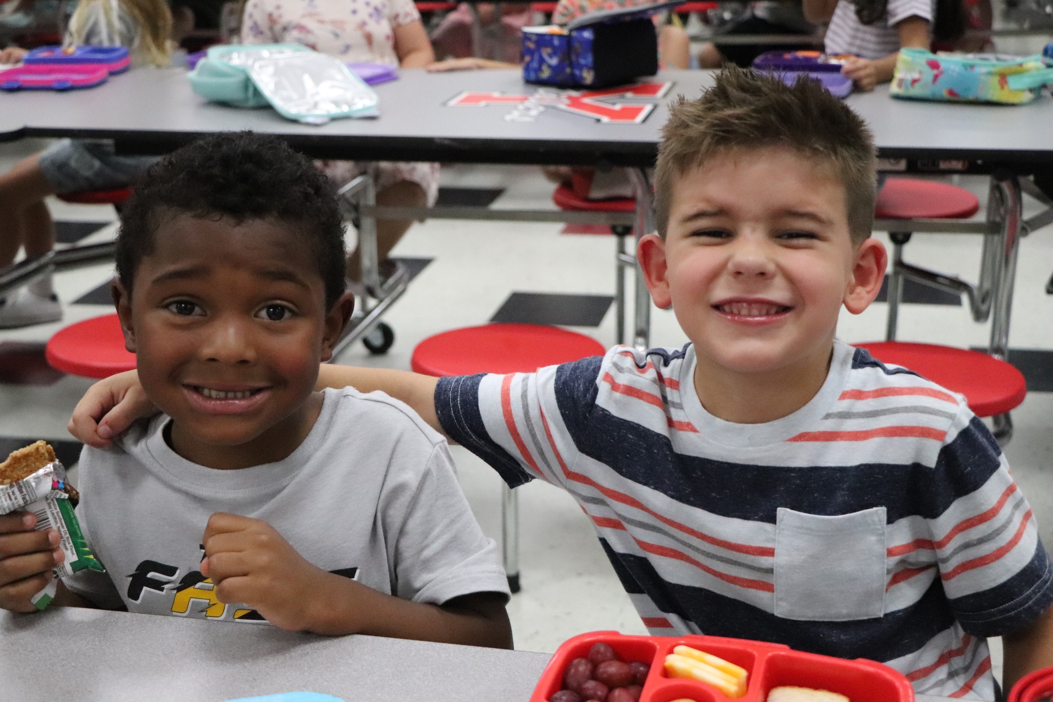 2 boys smiling in a cafeteria with their lunches