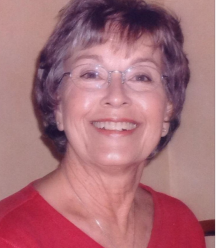 Woman with dark grey hair and glasses wearing red top smiling.
