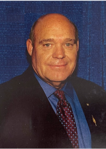 Man with no hair hearing a black sports coat, blue button down shirt, and burgundy tie