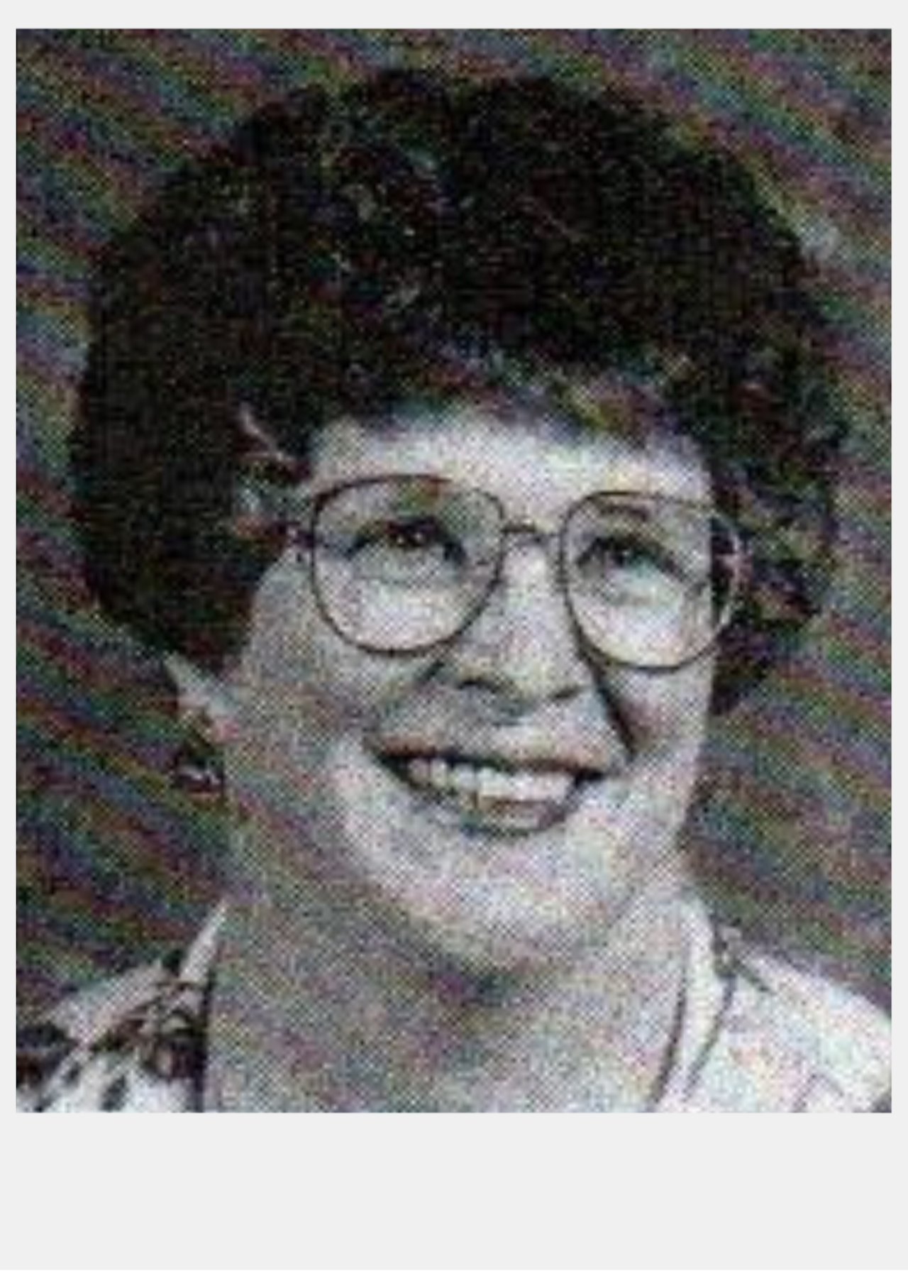 Black and white yearbook photo of a woman with short, dark curly hair wearing classes and a smile.