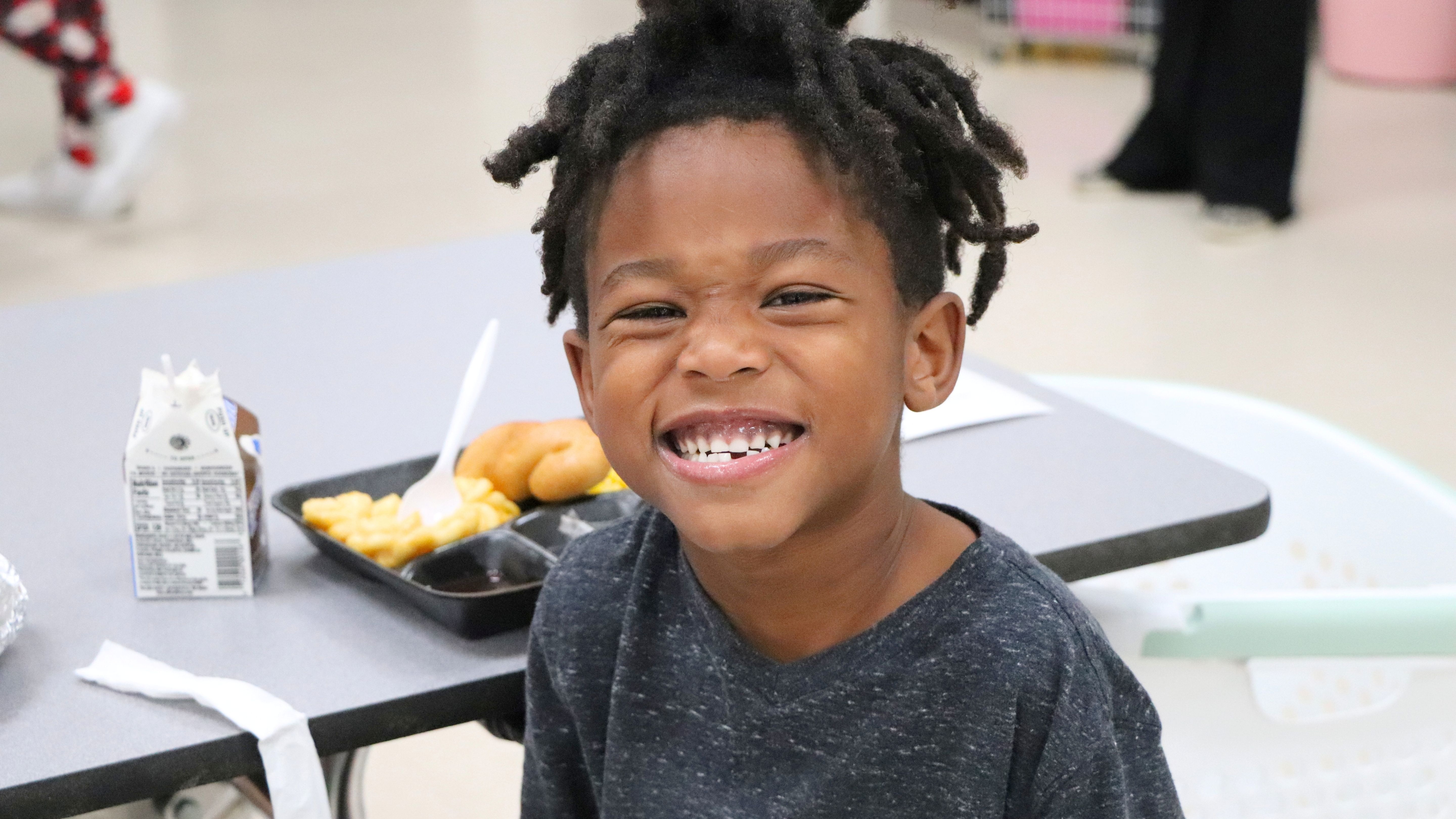 boy smiling in a cafeteria with his school lunch