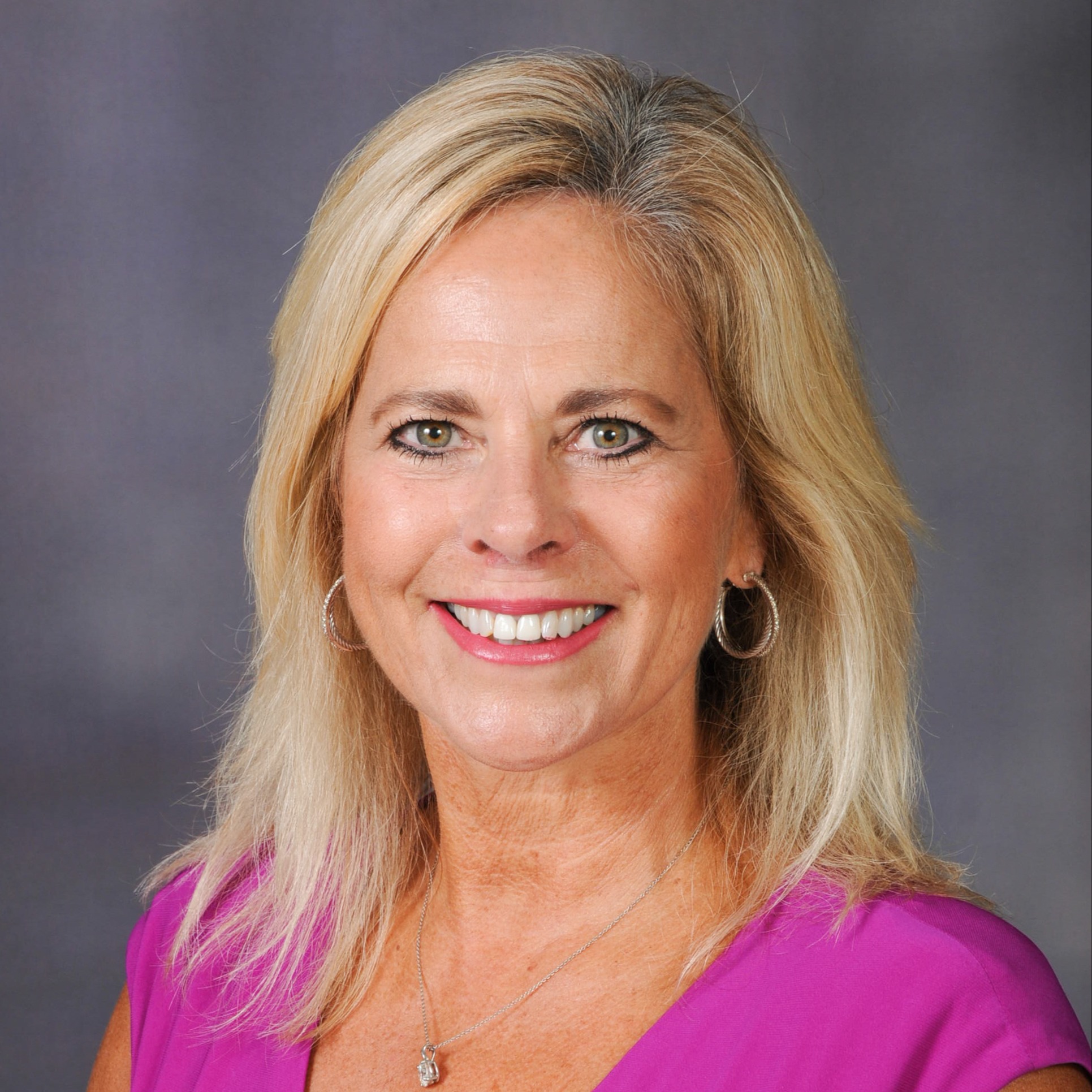 a woman with blonde hair and a pink shirt smiling at the camera