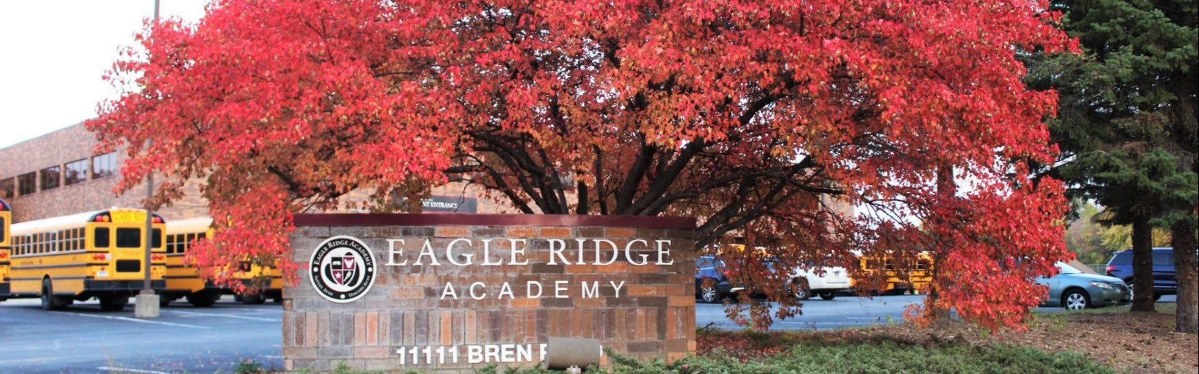 school building sign with fall tree behind it