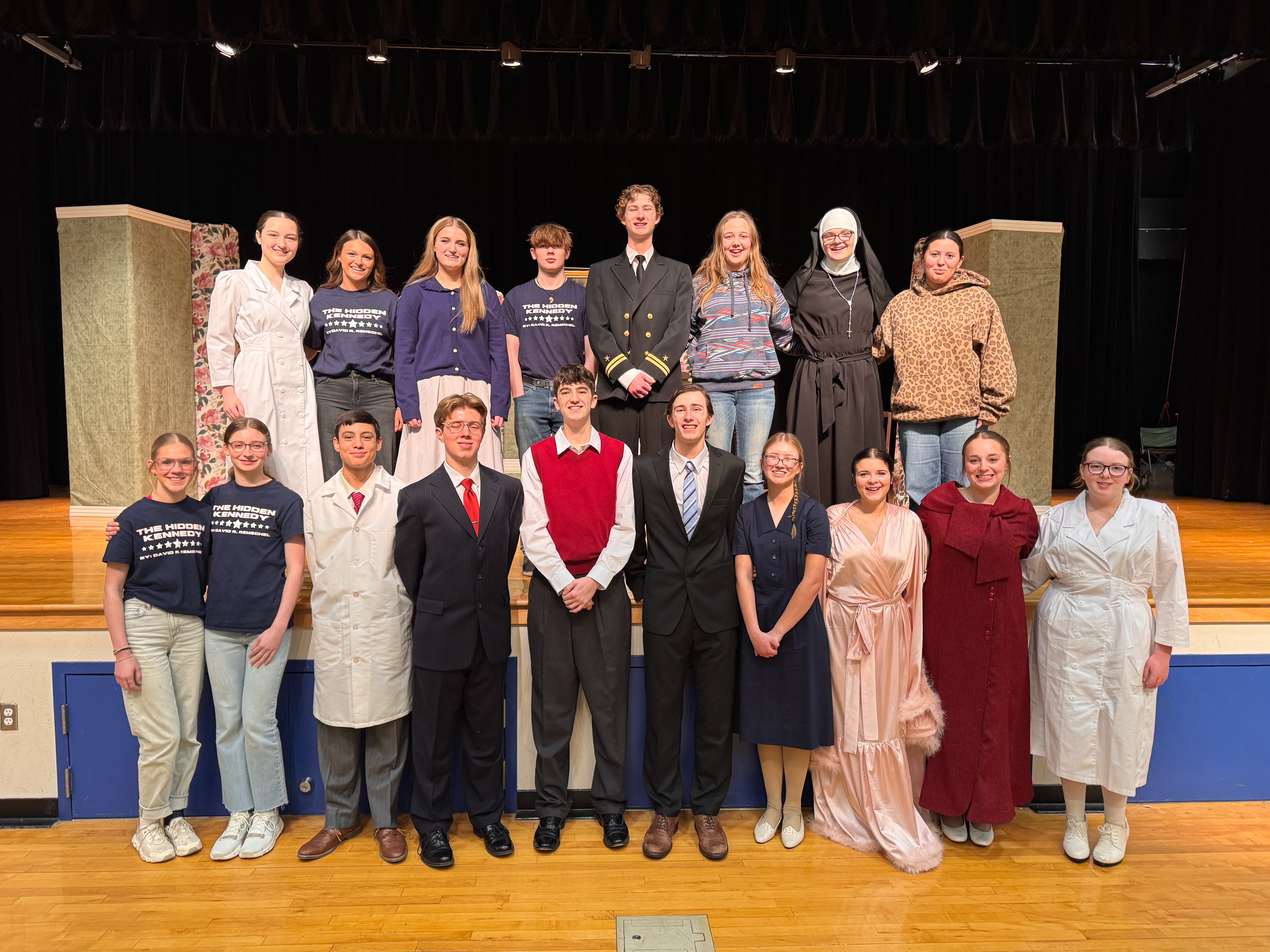 Students in cast in costume in a group photo on stage.